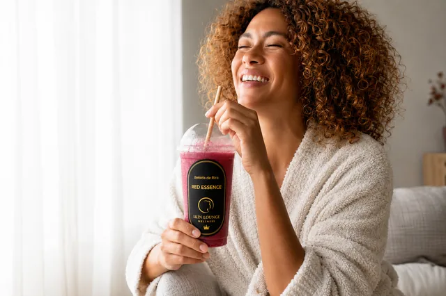 Mulher sorrindo com copo da Red Essence — smoothie funcional de frutas vermelhas Skin Lounge para proteção celular da pele